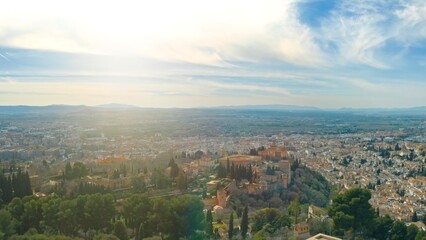 Naklejka premium Granada Spain aerial sunny panorama with Alhambra fortress surrounded by lush gardens city rooftops Andalusian landmark UNESCO World Heritage site with Sierra Nevada mountains horizon view traveling