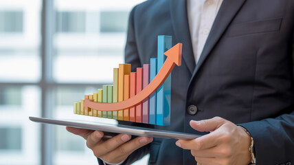 Businessman holding a tablet displaying a3D bar graph with an upward trending arrow business growth