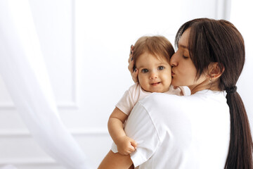 Loving mother kissing baby daughter at home, showing pure love