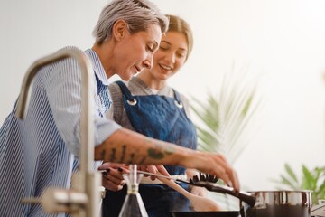 Low angle of mature woman with young daughter cooking on stove in kitchen and chatting in leisure