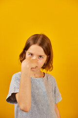 Child making a finger-pointing gesture against a bright yellow background during a playful moment