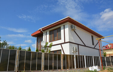 A modern half-timbered house with large panoramic windows, mosquito nets and sun blinds, a gutter, a metal roof, and a translucent fence.