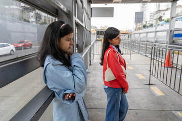 Two teenagers standing on a sidewalk, one wearing a blue jacket