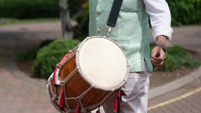 Close-up of a musician playing a dhol drum at an Indian wedding. Rhythmic beats, colourful tassels, and vibrant attire capture the joyful spirit of traditional celebration.