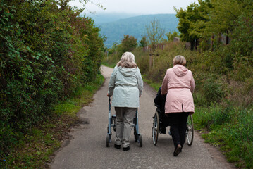 Elderly people taking a walk with help of walker with friends on a cold day through the park