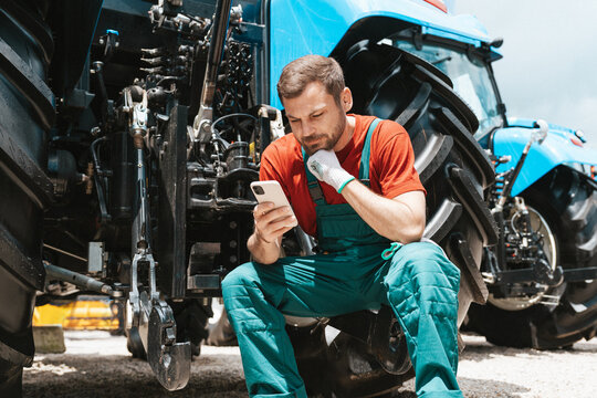 Rural man sitting near the agricultural tractor and checking his smartphone. - Powered by Adobe