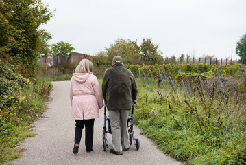 Elderly people taking a walk with help of walker with friends on a cold day through the park