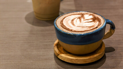 A beautifully crafted cup of hot chocolate with detailed latte art, served in a rustic ceramic mug on a wooden coaster