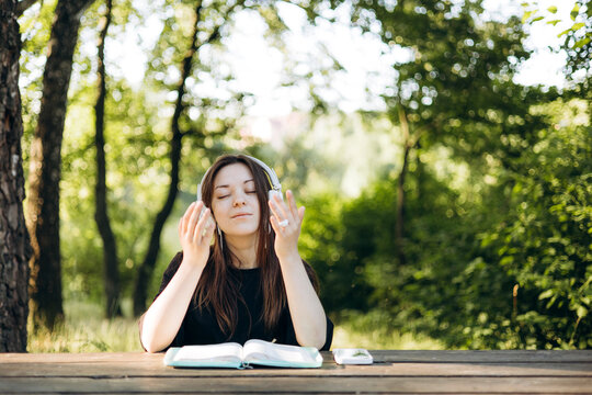 Young teen girl in headphones reading the Bible at a wooden table outdoors. - Powered by Adobe