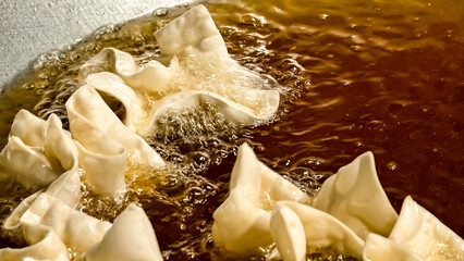 Wontons being deep-fried in hot oil, bubbling and cooking to a golden brown color.