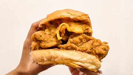 Close-up of a person holding a large chicken sandwich with cheese, on a white background.