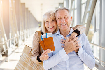 Smiling senior travelers embracing with passports and tickets at airport