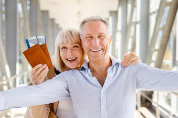 Cheerful senior couple taking selfie with passports at airport, ready for trip