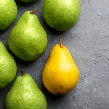 One yellow pear standing out in a group of green pears on a grey background. Minimal food concept.