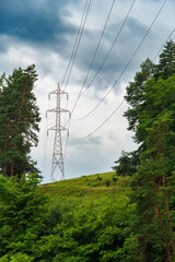 Obraz premium high voltage power line on a hill against the backdrop of forest and cloudy sky