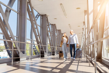 Mature couple walking hand in hand through airport corridor with suitcases