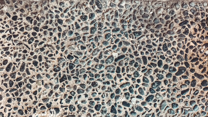 Close-up shot of a surface covered with small, dark pebbles embedded in a light-colored material, creating a textured pattern.