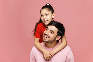 Fototapeta premium Young happy parent man with child girl she wear red casual clothes. Little kid daughter stand behind daddy hug embrace look aside isolated on plain pink background. Father's Day Love family concept.