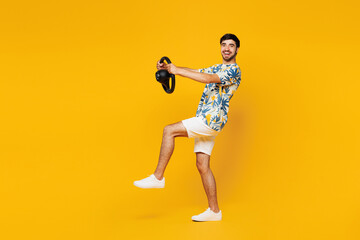 Full body young smiling happy man he wear blue beach t-shirt casual clothes hold steering wheel driving car raise up leg isolated on plain yellow orange background studio portrait. Lifestyle concept.