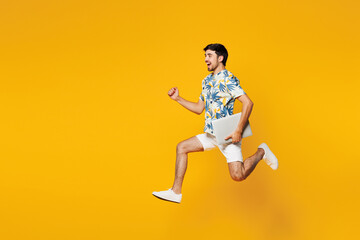 Full body side view young man he wear blue beach t-shirt casual clothes jump high run fast hold closed laptop pc computer isolated on plain yellow orange background studio portrait. Lifestyle concept.