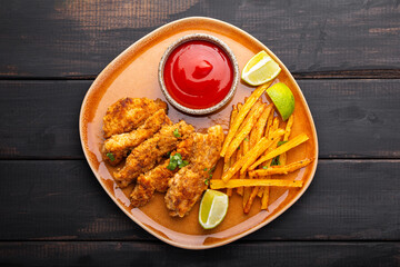 Homemade Crispy Chicken Strips with lime and ketchup and French Fries in a plate on a black wooden background. Top view