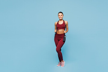 Full body young happy fitness trainer instructor sporty woman sportsman wear red sportswear train in home gym using hold skipping rope isolated on plain blue background. Workout sport fit abs concept.