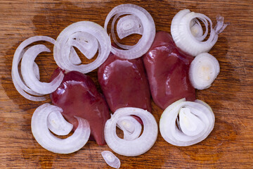 Freshly sliced liver and onions prepared on a wooden cutting board for a savory dish in a cozy kitchen setting