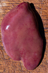 A unique close-up of shiny red-brown chicken liver on a wooden cutting board in bright natural light, taken at midday.