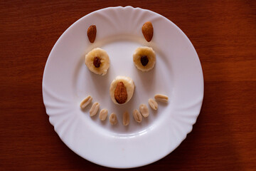 Creative food art featuring a smiling face made from fruits and nuts on a white plate