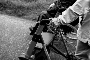 Obraz premium Elderly friends taking a walk in the park during cold weather with help of wheelchair and walker enjoying and having fun