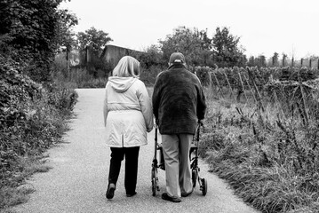 Elderly people taking a walk with help of walker with friends on a cold day through the park 