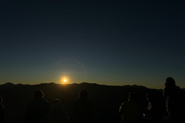 山の稜線に沈む夕日を眺める人々のシルエットと静かな感動の風景
