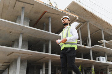 Engineer inspecting construction site with blueprint and walkie talkie