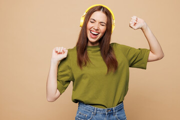 Young smiling happy woman wears olive green t-shirt casual clothes listen to music in headphones...