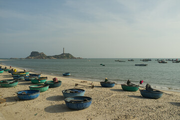 Ke Ga Lighthouse view on sea shore. Traditional Vietnamese basket boats on sandy beach. Calm sea waves with overcast sky