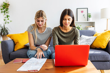 Two young happy female friends booking online their vacation trip, doing a reservation of their accommodation or flight with laptop and credit card