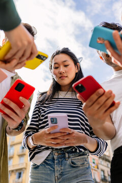 Young group of multiracial teen people using mobile phone device standing together outside