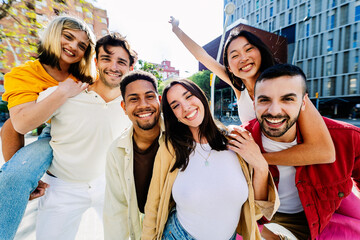 Portrait of diverse young friends having fun together outdoors in summer. Millennial student people laughing standing in city street enjoying holiday. Youth community and friendship concept.