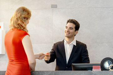 friendly hotel receptionist welcomes a guest at the front desk, offering excellent customer service and hospitality with a warm smile during check-in at a modern hotel lobby.