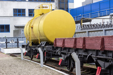 A yellow tank car and a flatcar with wooden sides are standing in railway dead end. Railroad freight transport.