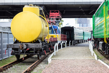 Rail transport at a station. yellow tank car and green passenger wagons.