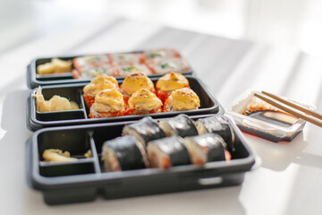 Assorted sushi rolls in takeout boxes with soy sauce and chopsticks on white table, japanese food delivery and lunch, concept of food