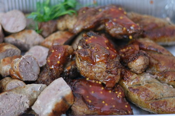 Close-up photo of mixed grilled meat platter. Beef, pork, poultry, sausages, grilled garlic, chili pepper, red tomatoes on wooden rustic background.