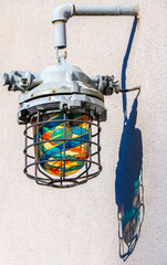 industrial outdoor lamp with colorful glass bulb and metal cage casting a shadow on wall