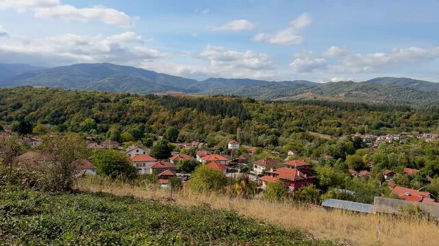 Panning shot of the town of Apriltsi from above against the backdrop of Stara Planina mountain. Red tiled roofs on houses. Panorama shot of Apriltsi. Scenic view.