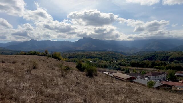 Panning shot of the town of Apriltsi from above against the backdrop of Stara Planina mountain and the peaks of Maragidik and Botev. Red tiled roofs on houses. Panorama shot of Apriltsi.