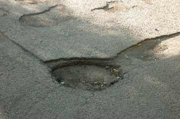 A pothole in cracked asphalt on an old, damaged road, showing wear and decay.