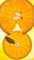 Two orange slices with a leaf against a yellow backdrop