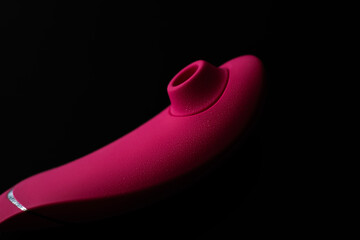 Close up of pink sex toy stimulator with water drops, placed against a blurred black background