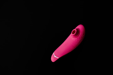 Close up of pink sex toy stimulator with water drops, placed against a blurred black background